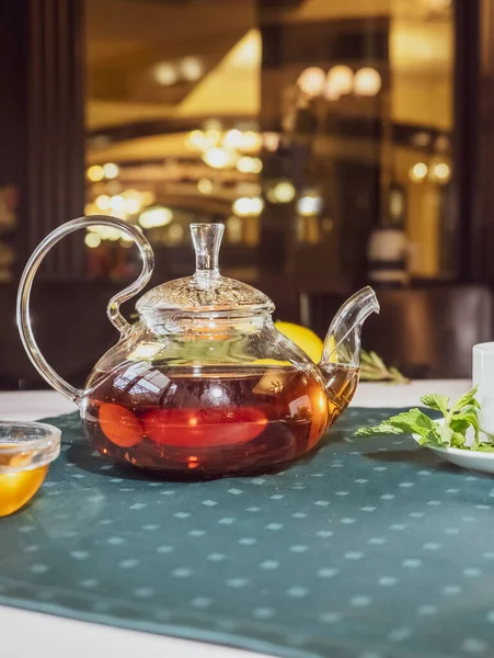蜂蜜と新鮮なミントの葉と暖かいぼやけた背景を持つガラスティーポットの芳香族ホット緑茶 カフェでお茶とテーブルを提供 — ストック写真