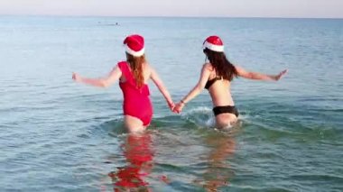 Anne ve kız Noel Baba 'nın şapkasıyla deniz kenarında eğleniyorlar.