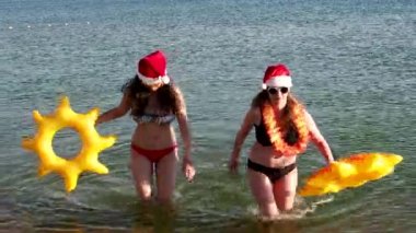 Noel Baba 'nın Şapkalı anne ve kızı, yeni yıl kutlamalarında ellerinde şişirilebilir yüzüklerle denizden yürüyorlar.. 