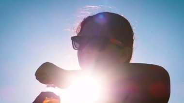 Güzel bir kadın sahilde şişede su içer.