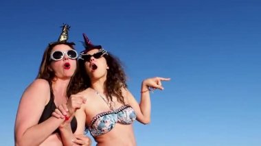 Anne ve kızı maskeli balo şapkaları ve gözlükleriyle deniz kenarında eğleniyorlar.