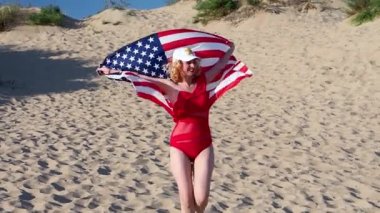 Kırmızı mayo giymiş bir kadın tropik bir plajda Amerikan bayrağı taşıyor.