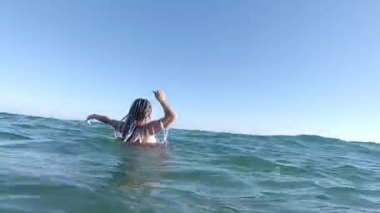 Kırmızı bikinili genç bir kadın denizde yüzüyor.