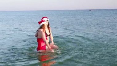 Anne ve kız Noel Baba 'nın şapkasıyla deniz kenarında eğleniyorlar.