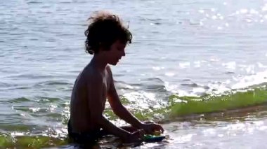 Sahildeki küçük çocuk. Gün batımında kumlu sahilde oynayan siyah saçlı kıvırcık saçlı çocuk. Çocuklar için yaz etkinlikleri