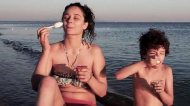 Siyah saçlı kız kardeş ve mayo giyen erkek kardeş yaz plajında piknik yapıyor ve kaşıklarla lezzetli meyve jölesi yiyorlar. Faydalı ve sağlıklı yiyecek kavramı..