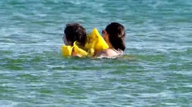 Siyah saçlı, sarı yelekli küçük bir çocuk ve genç bir kız kardeş sıcak denizde yüzerken eğleniyorlar. Suda çocuk aktiviteleri. Yaz tatili kavramı