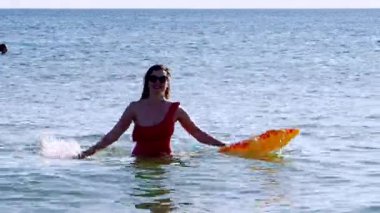 Kırmızı bikinili genç bir kadın denizde yüzüyor.