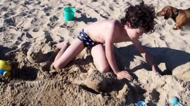 Küçük çocuk kumsalda kumdan kale yapıyor.