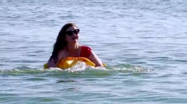 Kırmızı bikinili genç bir kadın denizde yüzüyor.