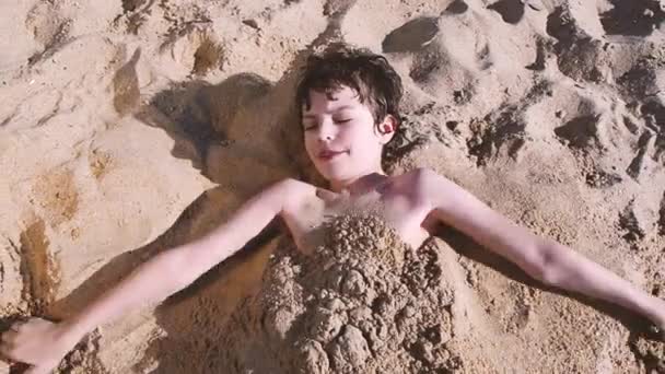 Liten Pojke Ligger Stranden Begravd Sanden Den Brunett Skrattande Pojken — Stockvideo
