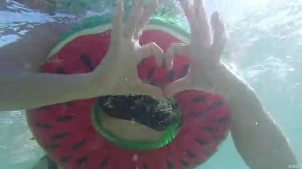 海に浮かぶ円を泳ぎながら手でハートサインをする女性 — ストック動画