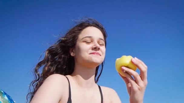 穿着黑色泳衣的布鲁内特少女坐在海边 吃着黄胡椒 健康的小吃和维生素食物 炎热的夏天和沙滩 湿透了乌黑的波浪般的头发 阿纳帕 — 图库视频影像
