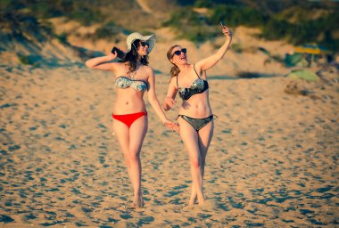 Anne ve kızı sahilde gülerek ve komik suratlar yaparak selfie çekiyorlar. Anne ve kızı genç esmerler sahilde cep telefonlarıyla fotoğraf çekiyorlar..