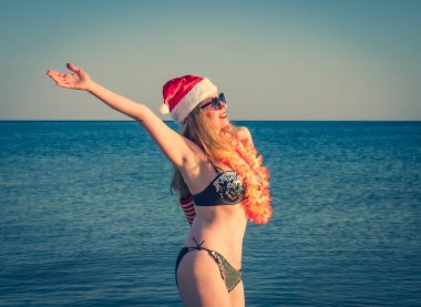Santa Hut 'ta güzel bir genç kadın, Hawaii aksesuarı ve sahilde bikini. Noel tatili Siyah parlak mayolu orta yaşlı bir kadın kumsalın tadını çıkarıyor