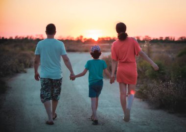 Siyah siluetler mutlu bir aile ve parkta yürüyen bir çocuk. Batan güneşin arka planına karşı ailesinin elini tutan küçük bir çocuk. Aile mutluluğu kavramı