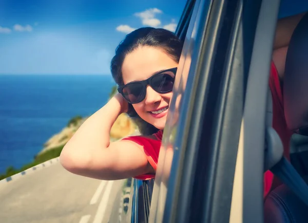 The girl leaned out of the car window. Drive along the coast. summer vacation, vacation, travel, road trip and people concept - happy teenage girls or young women in car at sea