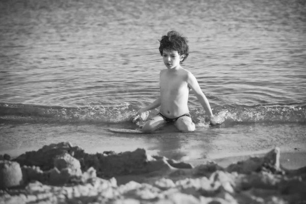ビーチでかわいい巻き男性の子供はゲームをプレイします 夏のビーチで砂で小さな男の子は遊びます 子供は海岸で楽しんでいます レジャー ゲーム 黒と白の写真 — ストック写真