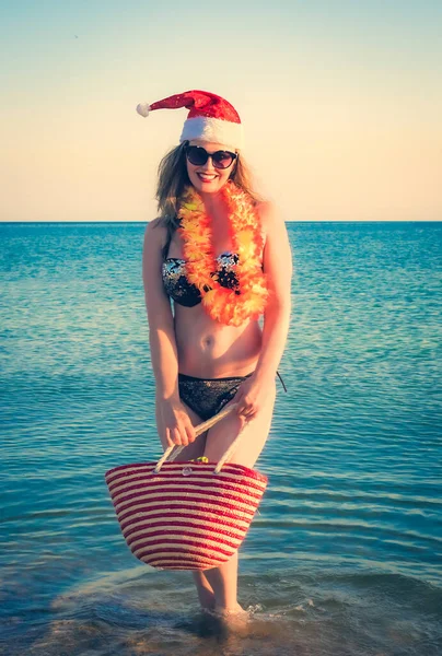 サンタハット ハワイのアクセサリー ビーチでビキニの美しい若い女性 クリスマス休暇かわいいです中年女性で黒光沢のある水着楽しんで砂トロピカルビーチ — ストック写真