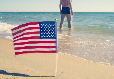 Amerikan vatanseverliği ve kumlu bir sahilde Amerikan bayrağı. Arka planda erkek gövdesi
