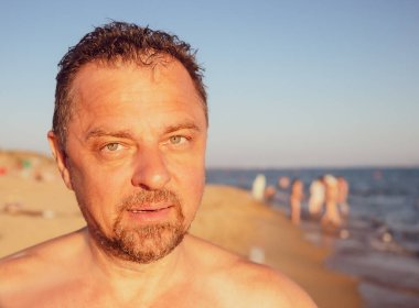 Sahilde kameraya bakan orta yaşlı bir adamın portresi..