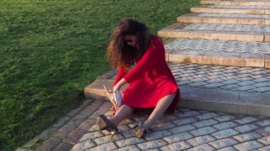 Kırmızı elbiseli sarhoş bir bayan mezuniyetten sonra merdivenlerde oturuyor ve tökezliyor. Çantada bir şey arıyor. 