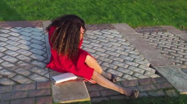 Mezuniyetten sonra merdivenlerde oturan kırmızı elbiseli, sarhoş ve zarif bir bayan.