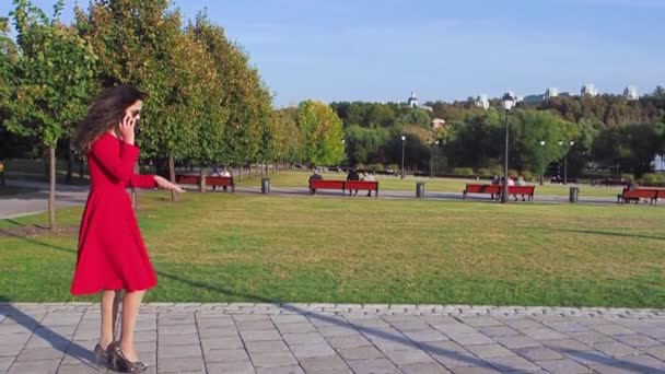 穿着红色衣服的优雅女士在公园里走来走去 接电话 动作缓慢 — 图库视频影像