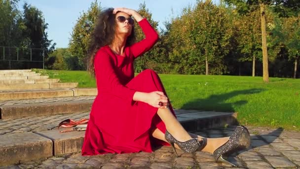 穿着红色衣服的优雅女士在公园里的包里找电话 — 图库视频影像