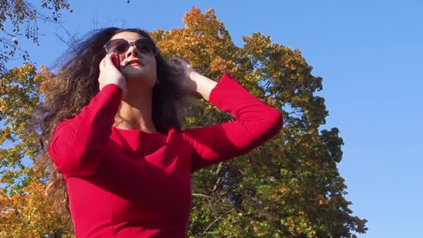 穿着红色衣服的优雅女士拿着电话在公园里微笑 — 图库视频影像