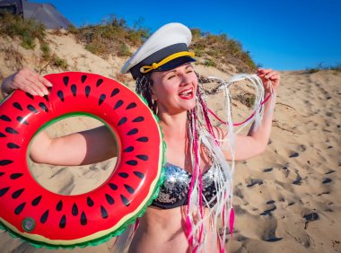 Güzel, orta yaşlı, saçları örülü ve kumlu bir plajda gülen subay şapkası olan bir kadın. İyi tatiller.