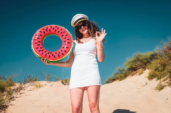 Girl in an officer\'s cap on beach. Young woman having fun making gestures ok outdoor in the summer.