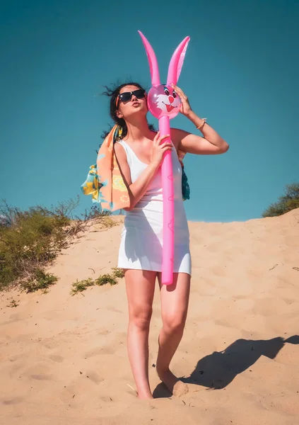 브루넷 해변에서 재밌게 여자가 부풀어 오르는 분홍색 토끼와 재미있게 즐기고 — 스톡 사진