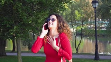 Genç bir kadın telefonda konuşuyor ve parkta birine el sallıyor.