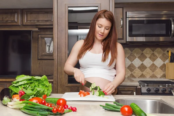 Беременная женщина режет огурец для салата — стоковое фото