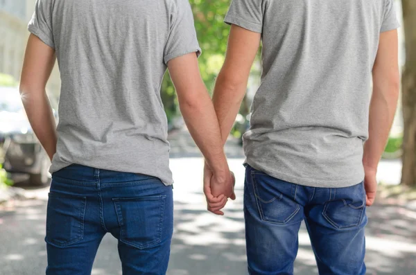 Два гомосексуальных парня, идущих по улице весной, изображают, как они счастливы улыбаясь и обнимаясь — стоковое фото
