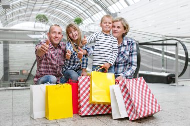 Başparmak gösterilen alışveriş merkezinde alışveriş torbaları ile aile 