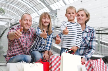 Başparmak gösterilen alışveriş merkezinde alışveriş torbaları ile aile 