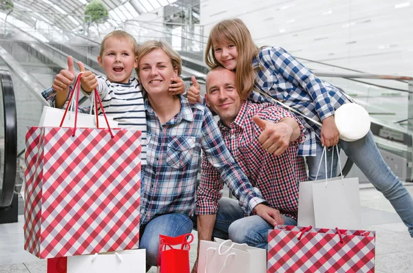 Familia con bolsas de compras en el centro comercial mostrando pulgares — Foto de Stock