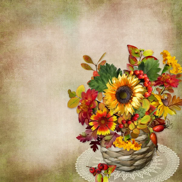 Аромат осенних цветов, листьев и ягод в плетеной корзине на винтажном фоне — стоковое фото