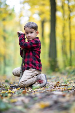 Güzel küçük çocuk ormanda sopayla oynuyor kameraya bakıyor.