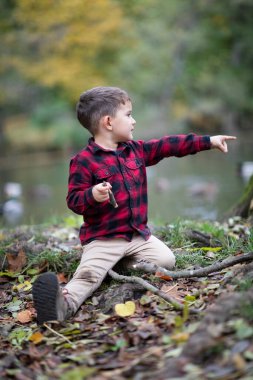 Güzel küçük çocuk bir ormanda yerde oturmuş bir şeyi işaret ediyor.