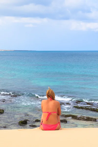 Mujer joven sentada en la playa mirando al océano y el cielo, B — Foto de Stock