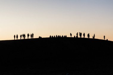Çin 'in Gansu Eyaleti yakınlarındaki Singing Sands Dune' da turist siluetleri