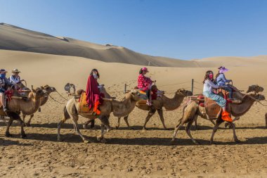 DUNHUANG, Çin - 21 Ağustos 2018: Turistler Çin 'in Gansu Eyaleti yakınlarındaki Singing Sands Dune' da deveye biniyorlar