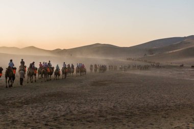 DUNHUANG, Çin - 21 Ağustos 2018: Turistler Çin 'in Gansu Eyaleti yakınlarındaki Singing Sands Dune' da deveye biniyorlar
