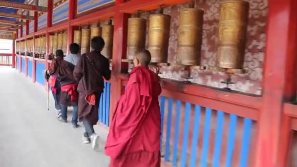 XIAHE, KINA - AUGUST 24, 2018: Människor passerar en rad av be hjul runt Labrang kloster i Xiahe stad, Gansu provinsen, Kina — Stockvideo