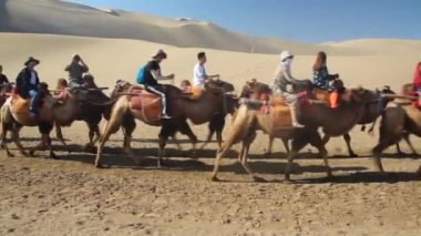 DUNHUANG, Çin - 21 Ağustos 2018: Turistler Çin 'in Gansu Eyaleti yakınlarındaki Singing Sands Dune' da deveye biniyorlar
