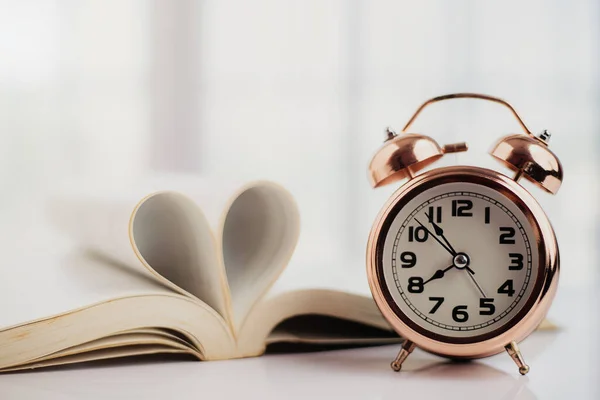 Bell alarm clock and opened book with heart shaped page on the table for study, work, time management and love concept