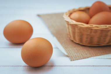 Hasır sepetteki yumurtalar sağlıklı yiyecek konsepti için beyaz ahşap arka planda.